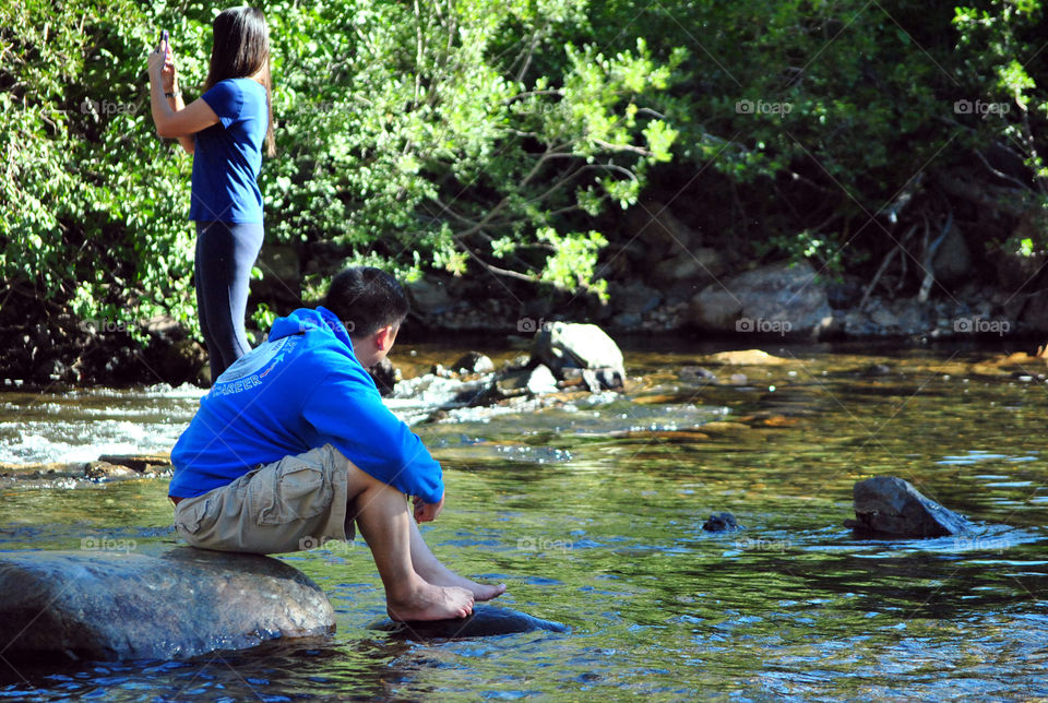 photo story, man relaxing and a girl taking a photograph using mobile phone at the waterfalls stream