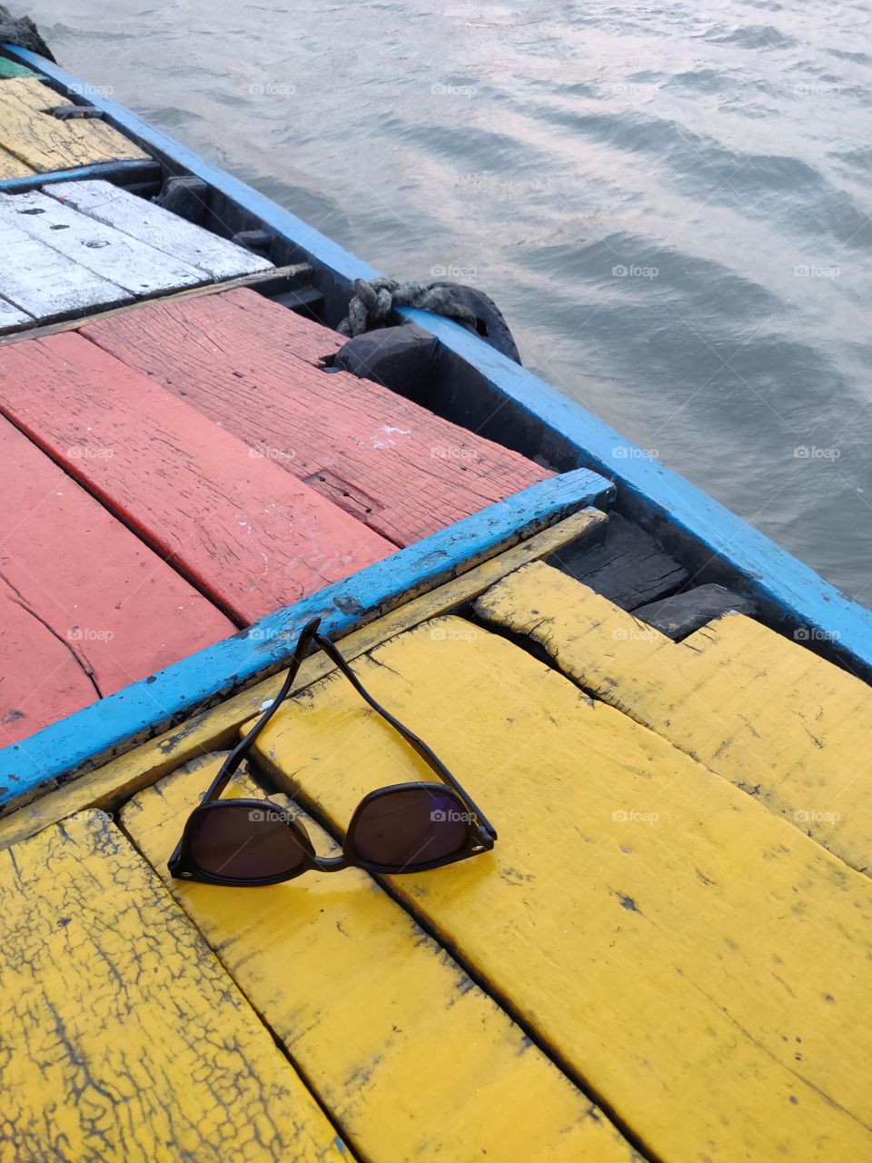 black sunglasses kept on a colorful deck of a wooden boat floating in the water