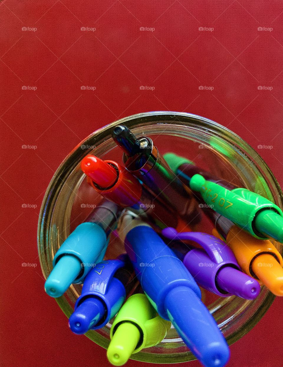 Overhead closeup of glass mason jar holding color pens on flat red surface 