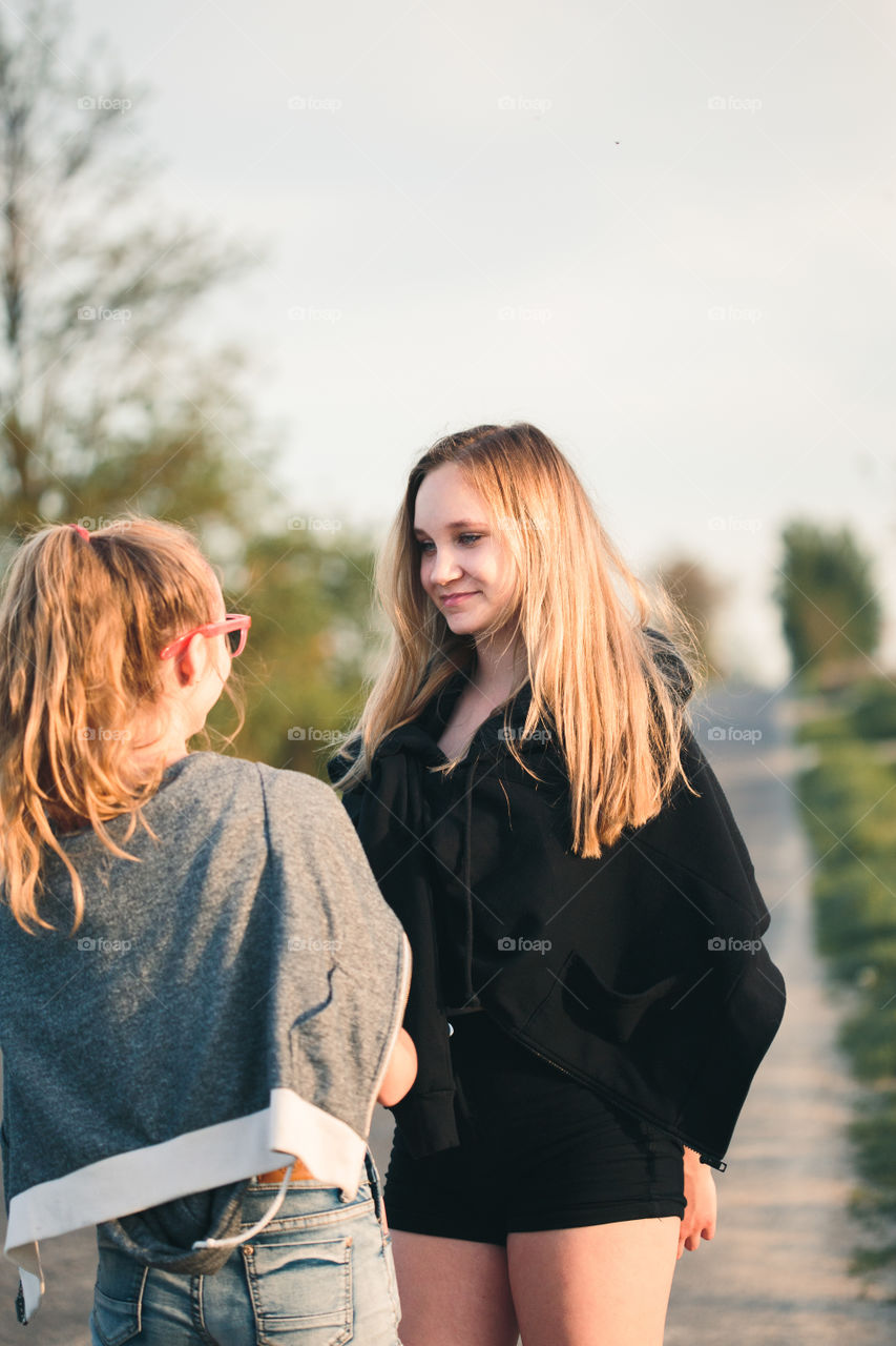 Teenage smiling happy girls having fun walking outdoors, hanging, spending time together on summer day. Real people, authentic situations