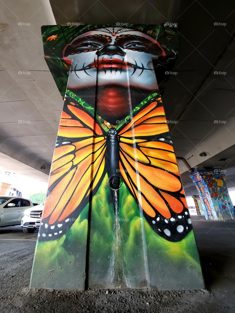 Street art: Dia de los muertos portrait with a large monarch butterfly on a cement highway pillar underpass. Also known as day of the dead, a Mexican cultural celebration and remembrance of those that have passed. Street art artist: @PauLGars0n13