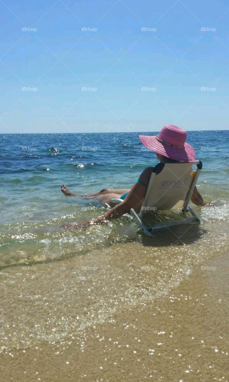 Woman wearing hat sitting on chair in the sea