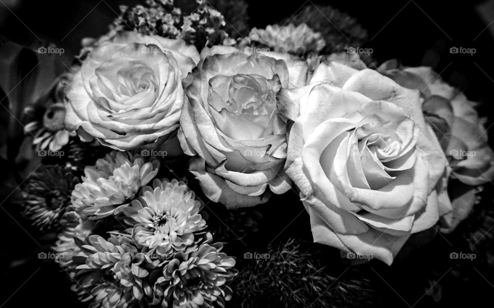 A black and white photo of a bouquet of flowers. There are roses, mums, and lilies.