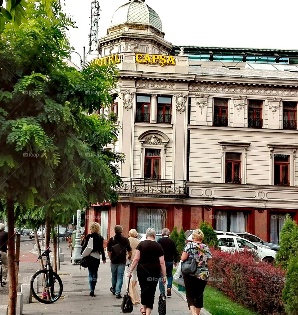 People carrying bags walking past the Capsha Hotel, one of the oldest hotels in Bucharest