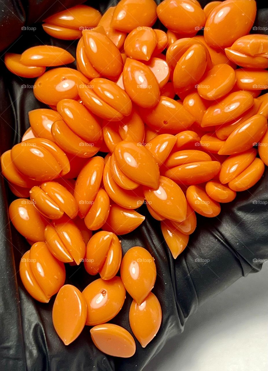 Orange hot wax for depilation in granules on a dark background. 