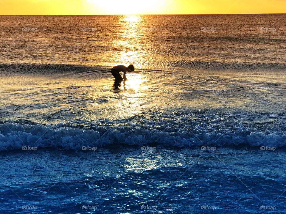 Small boy playing in the ocean in the golden reflection of a late summer sunset.