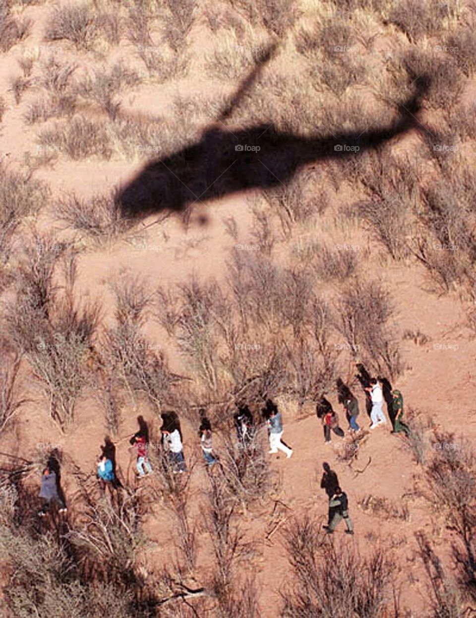 The shadow of a Blackhawk helicopter hovers above a group of illegal