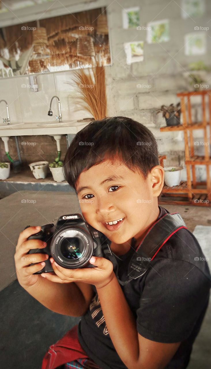 Model camera Canon 550D model anak laki laki baju hitam membawa kamera Canon 550D