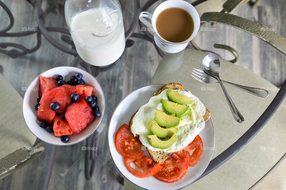 Healthy breakfast of whole grain toast, egg whites, avocado, tomato, watermelon, blueberries, milk, and coffee