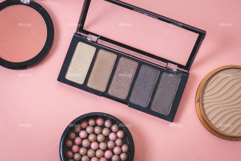 A set of cosmetics from one palette of nude eye shadow and three round face powders on a pink background, flat lay. Concept female cosmetics, beauty salon.