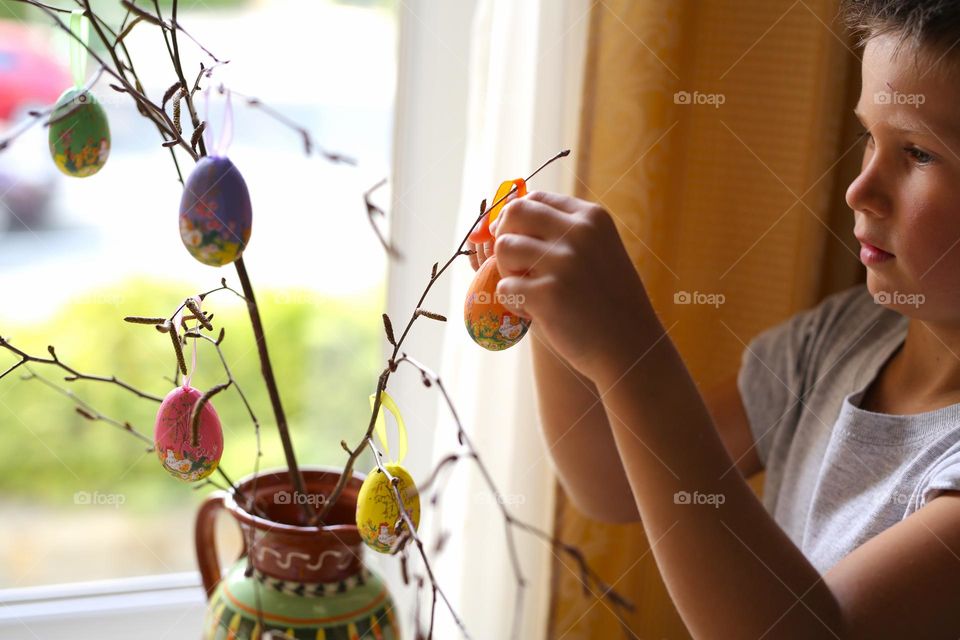 a boy of seven years old, paints crafts at home, Easter eggs, the boy is preparing for the holiday.  home crafts, craft activity.  a child decorates a tree branch with homemade eggs for Easter