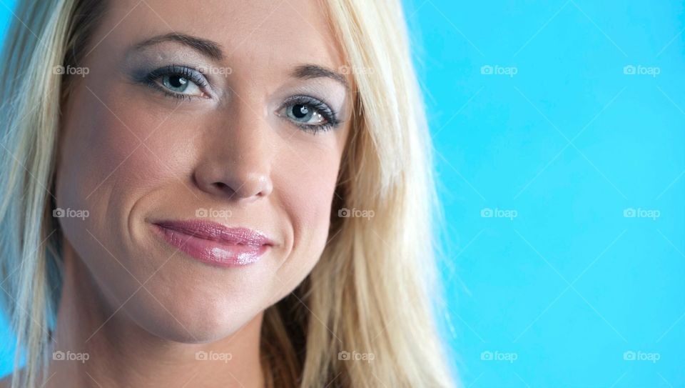 Blonde girl with blue eyes on blue background. Closeup Portrait. 