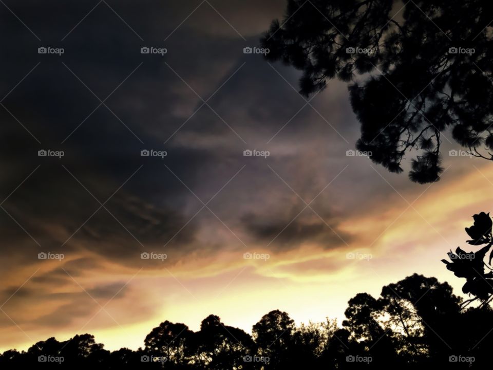 Dark storm clouds descend upon a golden sunset.