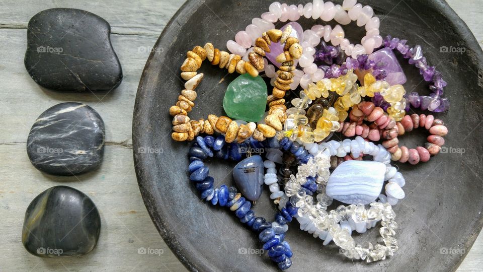 Gem stones in a black bowl on a grey wooden background with zen stones