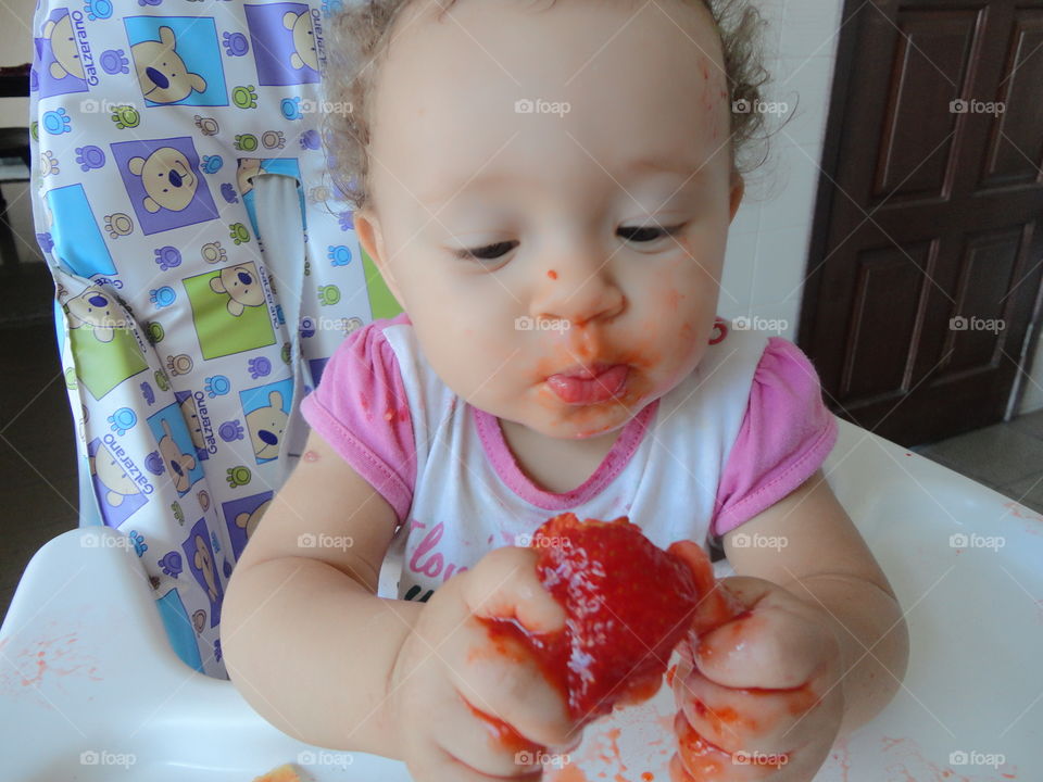 Baby sitting in high chair smashing red food