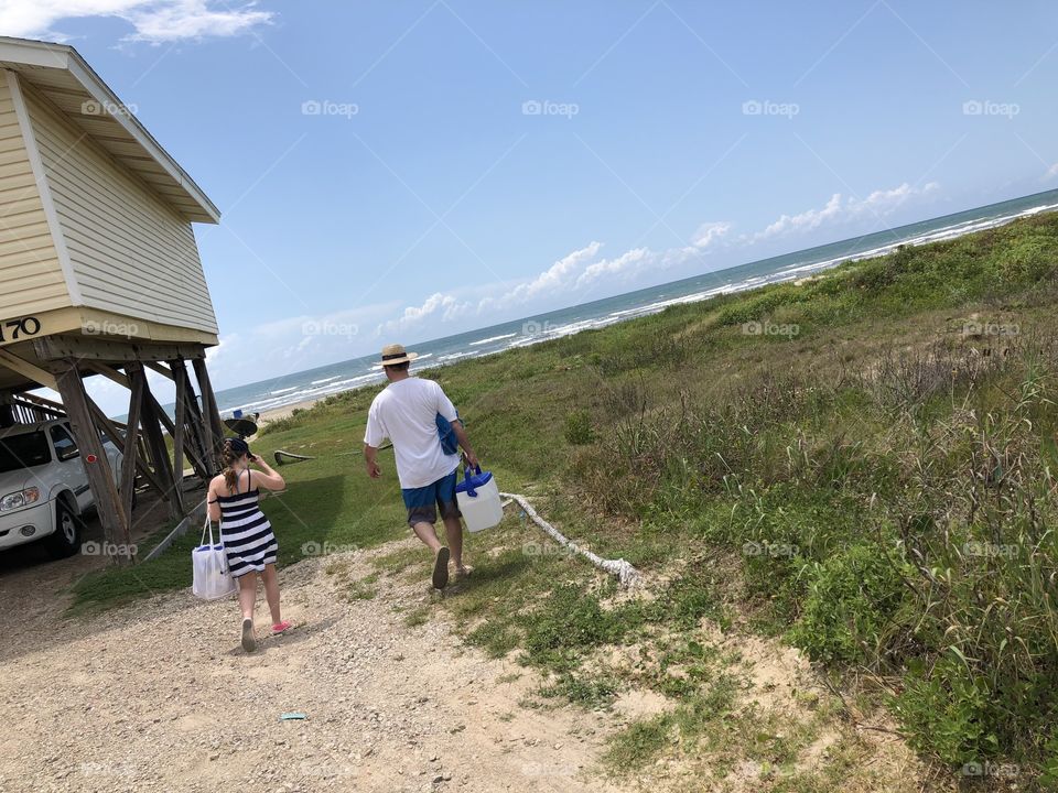 Father and daughter walk by beach house to have a picnic with a cooler