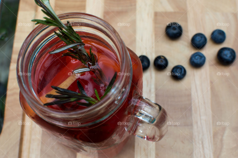 Aromatic berry flavored lemon water with fresh rosemary herbs and antioxidant rich blueberry and raspberry in retro style glass jar mug elevated view on wood table with Strawberry garnish 