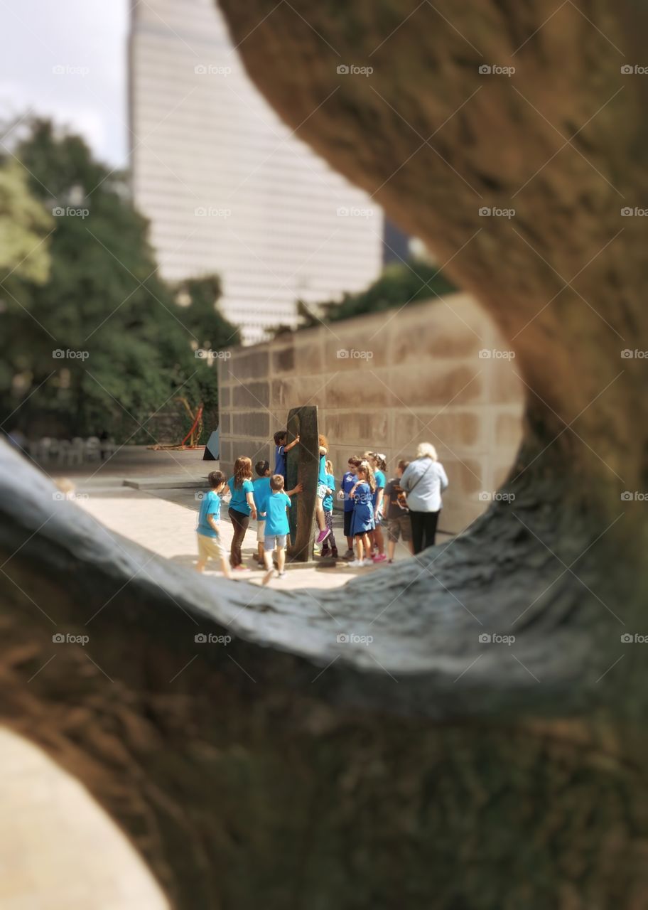 Kids playing on an outside art sculpture at a museum in Dallas Texas framed through another sculpture