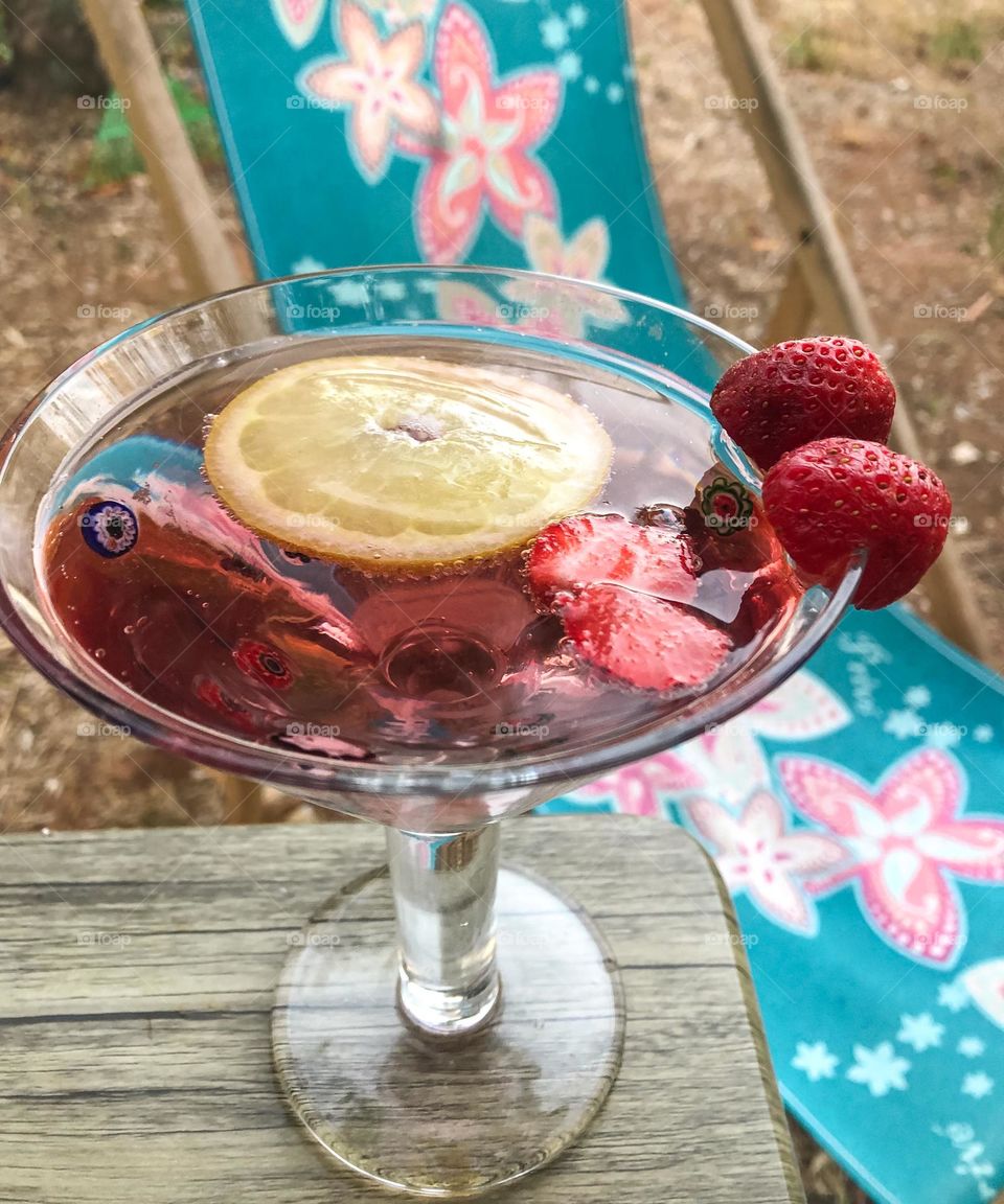 A summer drink with lemons and strawberries in front of a colourful deck chair