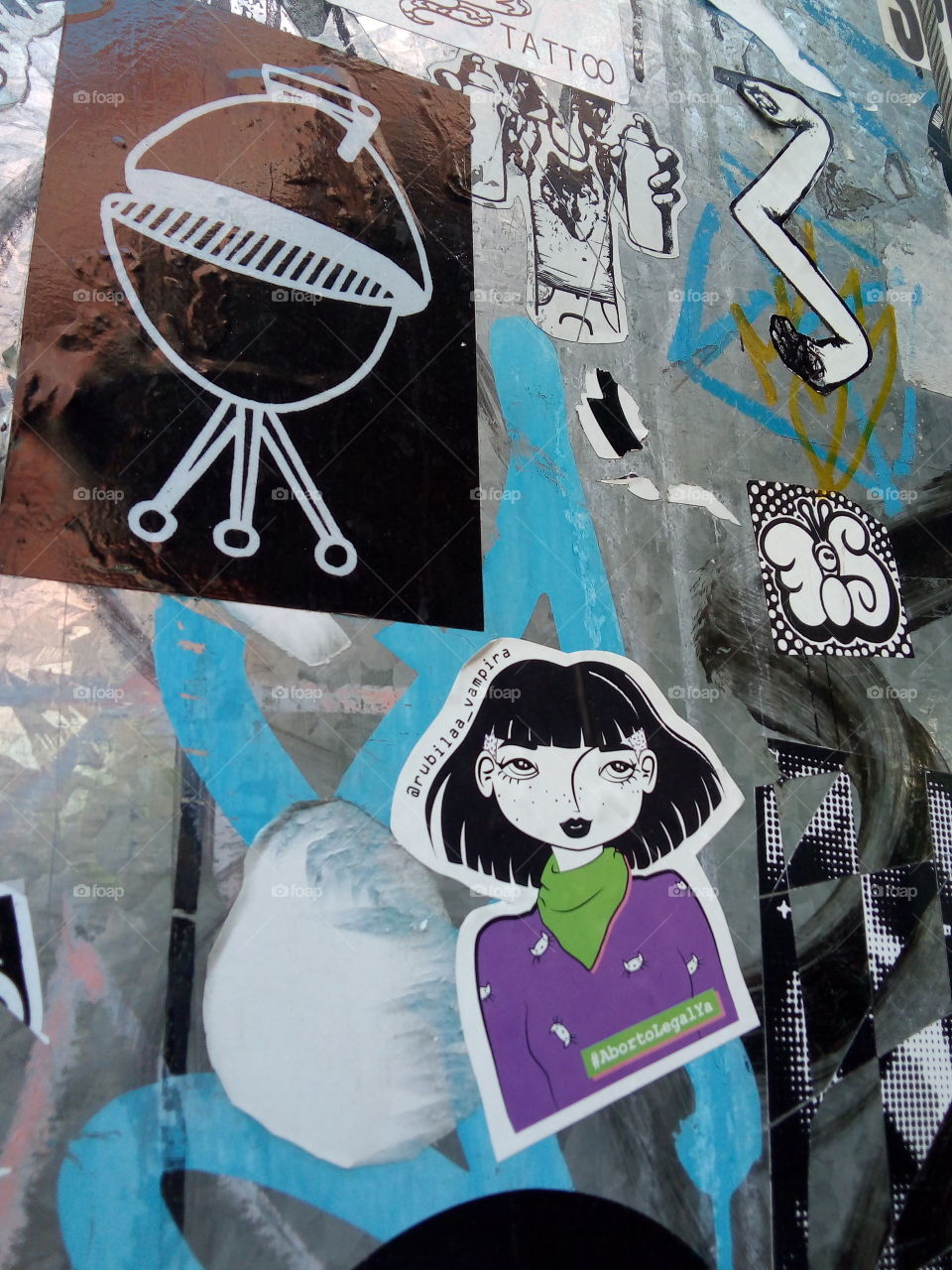 fotografía de pared con stickers pegados o estampas mostrando mujer con cabello negro, parrilla, etc