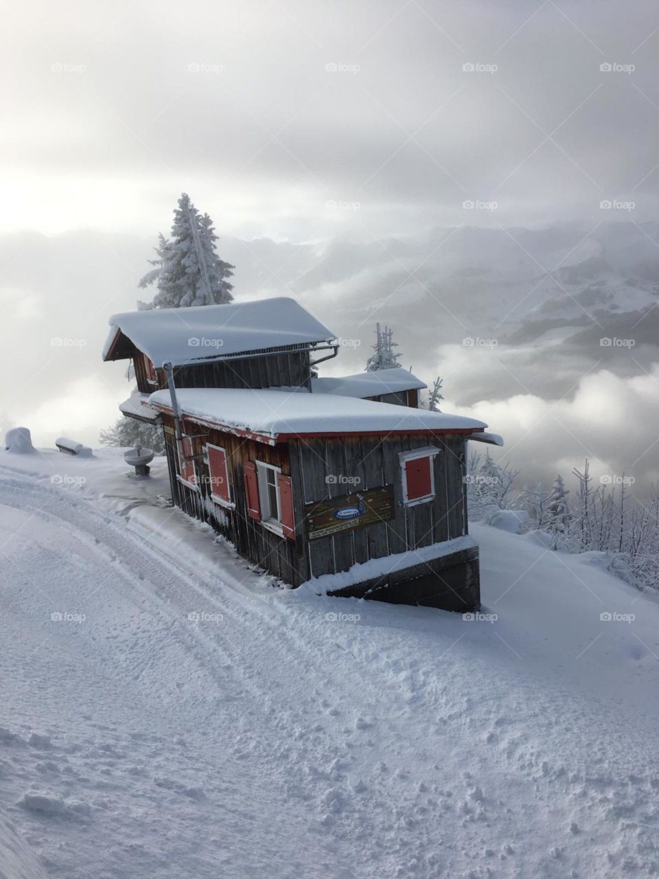 a house with many red windows,white snow covered on a roof,trees and the mountain surface.The mountains in the distance could not be seen clearly, clouds and fog filled the sky and mountains