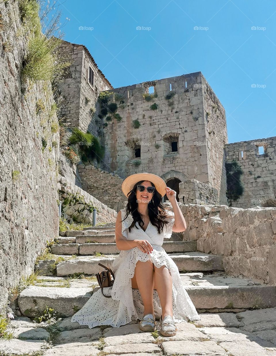 Portrait of happy young woman sitting on stone steps of an medieval fortress at Klis near Split, Croatia