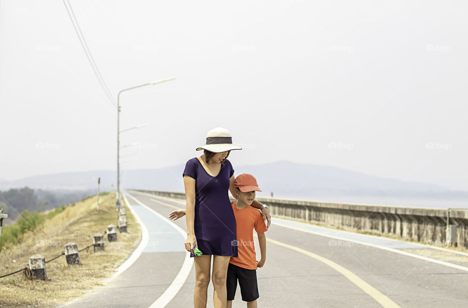 Portrait of a mother and son walking on the street Background mountains and water at Krasiew dam ,Supanburi Thailand.