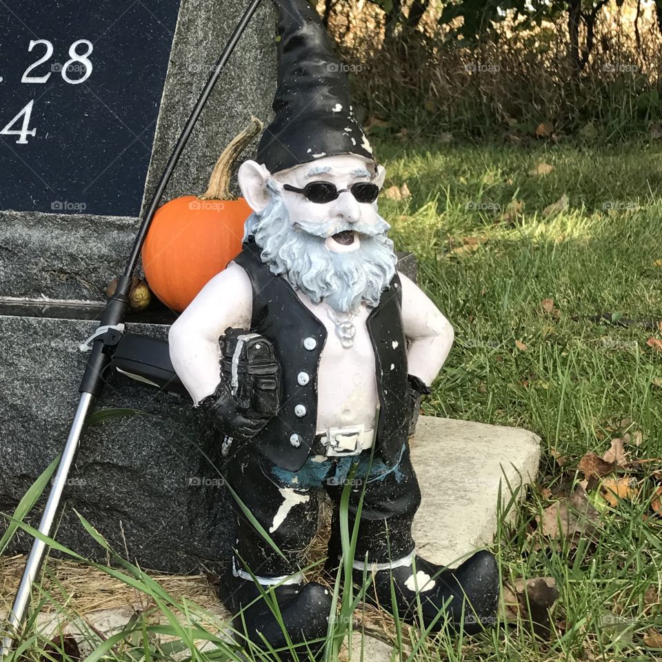 Gnome dressed like a biker standing next to a gravestone.