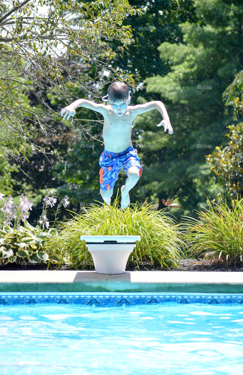 Young boy jumping into an inground swimming pool from a diving board