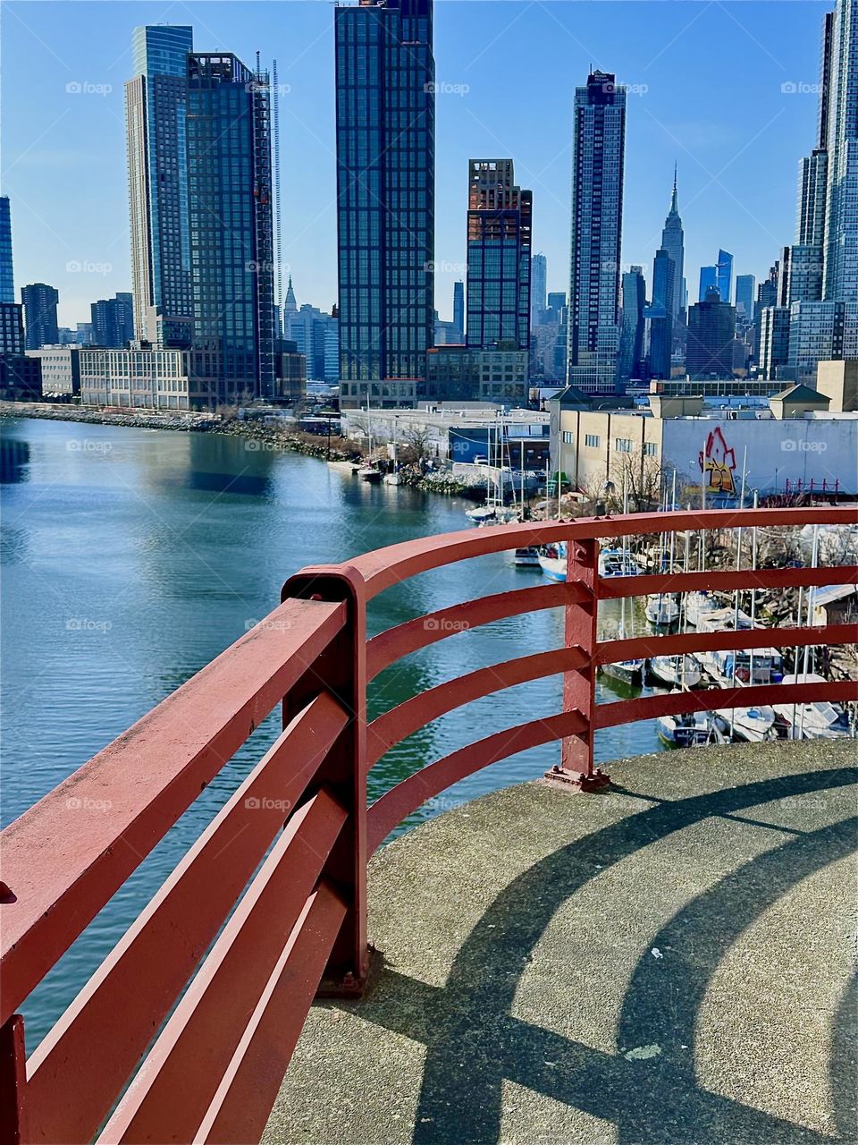 The curvy structures such as the red metal railing of the central outpost of the “Pulaski Bridge” at “Newtown Creek” that connects “Greenpoint”, Bklyn to LIC makes a striking motif that is further enhanced by its shadows. 2024. Hypnotic Productions