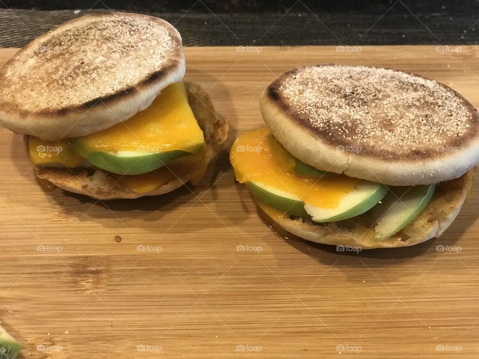 Display of two delicious English muffin sandwiches with melted cheese and apple slices inside displayed on a cutting board in the kitchen prepared for lunch. USA, America 