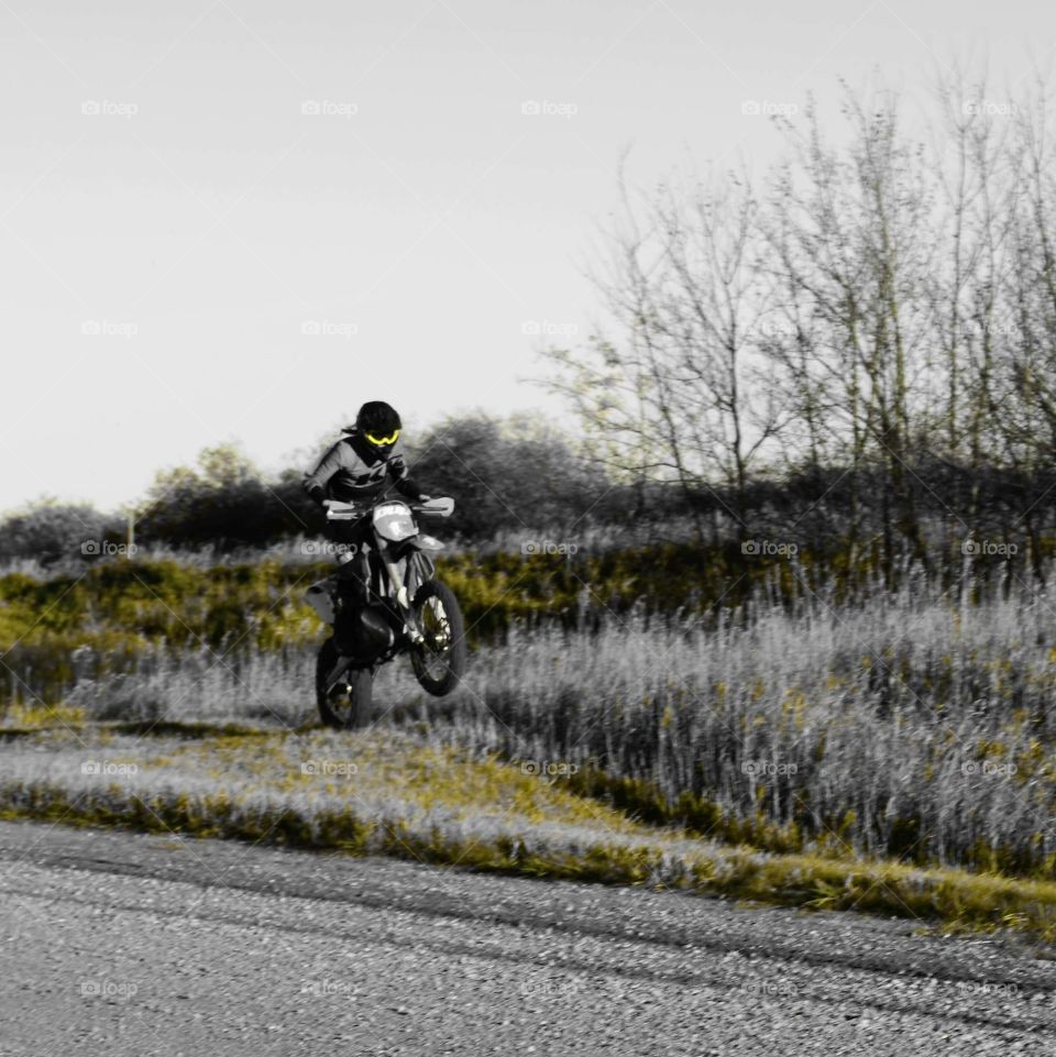 Dirt bike rider jumping an approach in a ditch down a country gravel road. 