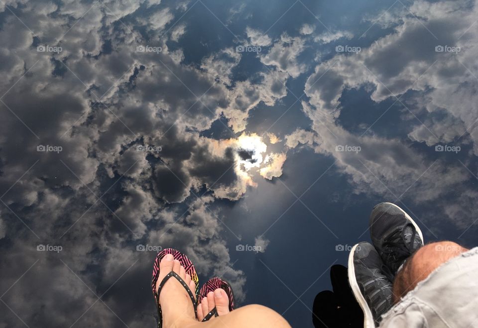 Legs dangling over a pool of water reflecting the sun through a cloudy sky
