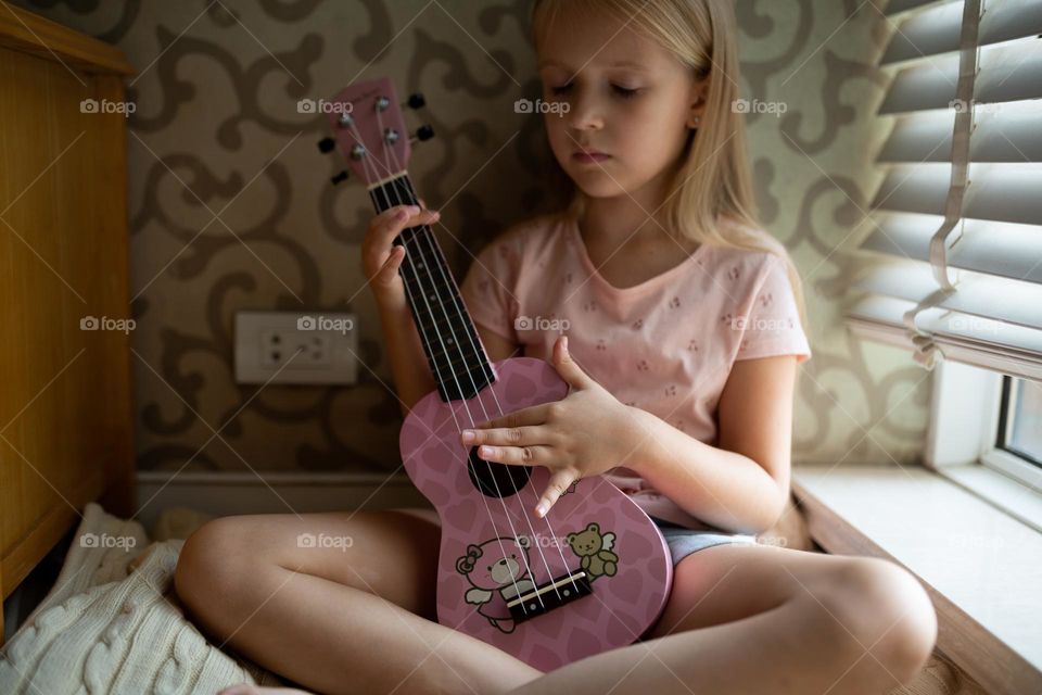 Little Caucasian girl playing on ukulele at home