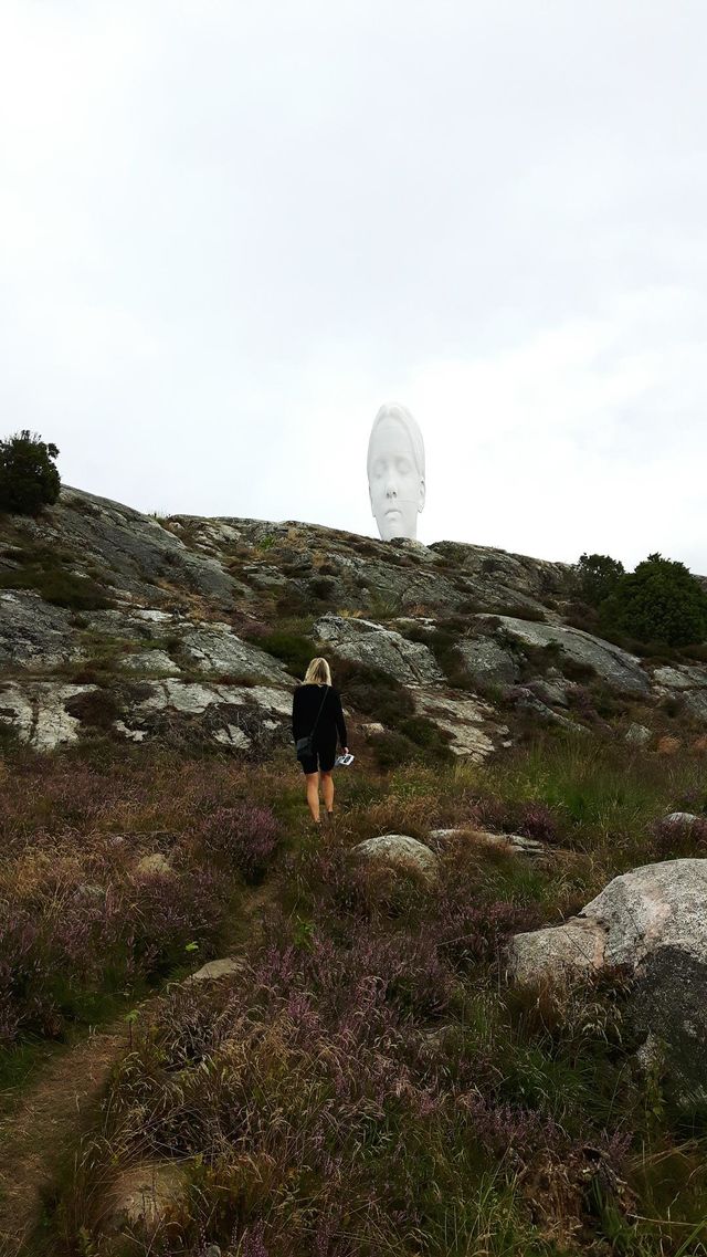 Woman walking up a hill towards a white sculpture head
