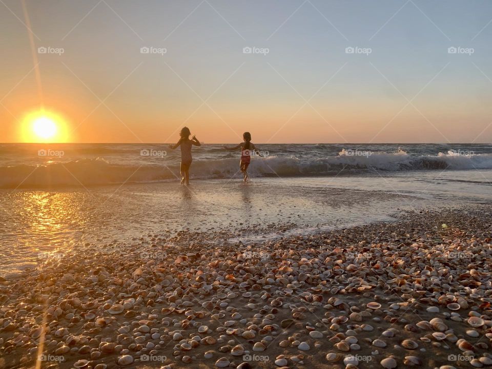 Two girls playing in the surf during sunset on a beach full of sea shells 