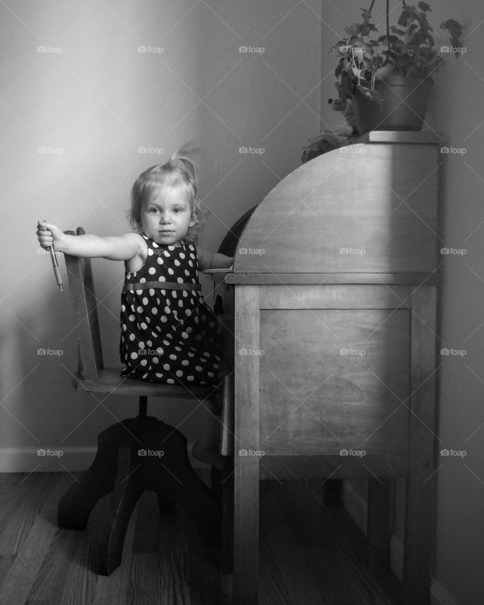 A black and it's photo of a young child writing and her desk.