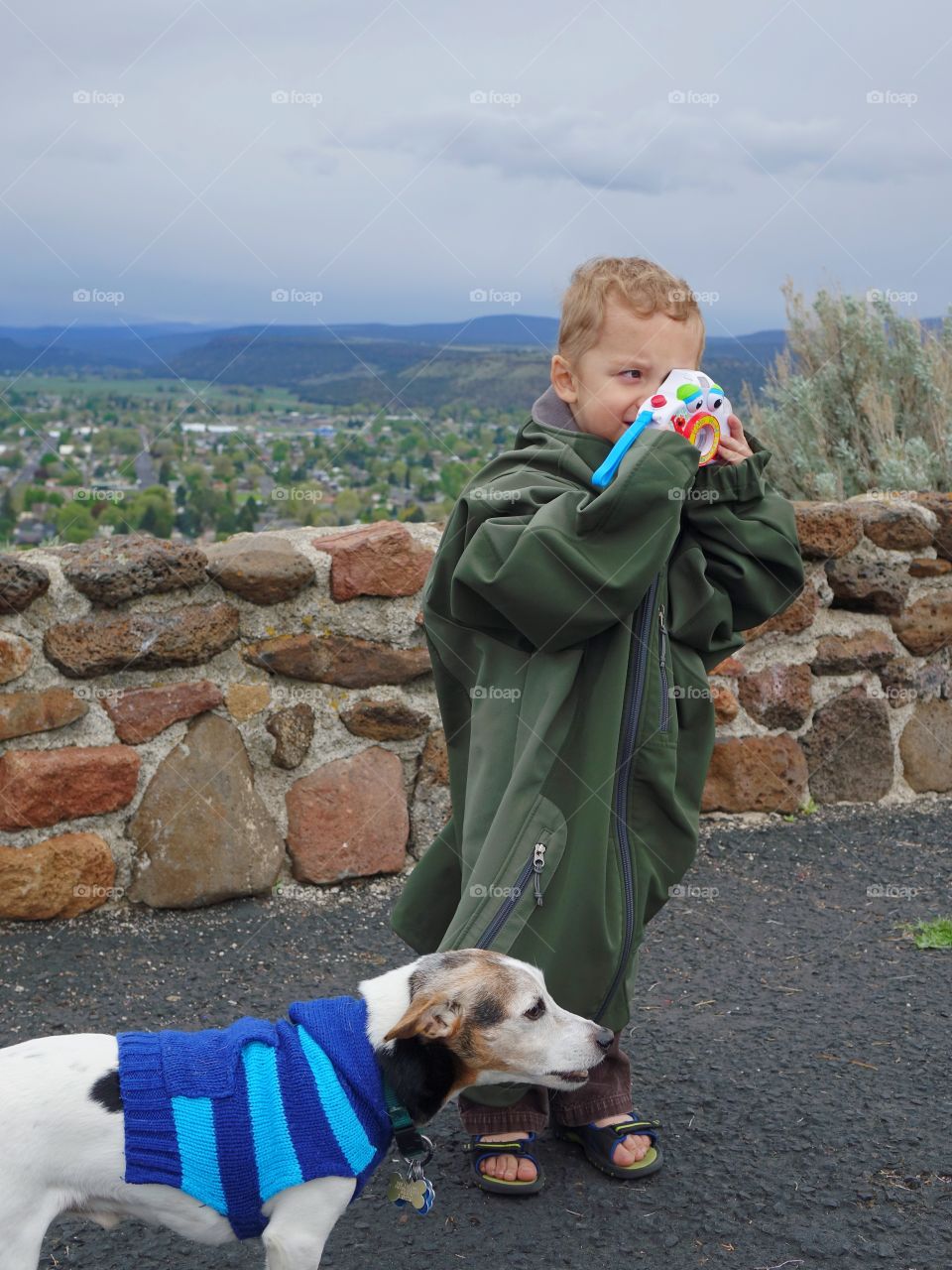 A cute little boy with his toy camera draped in an adult coat with his little Jack Russell Terrier adorned with a sweater in Central Oregon on a chilly spring day. 