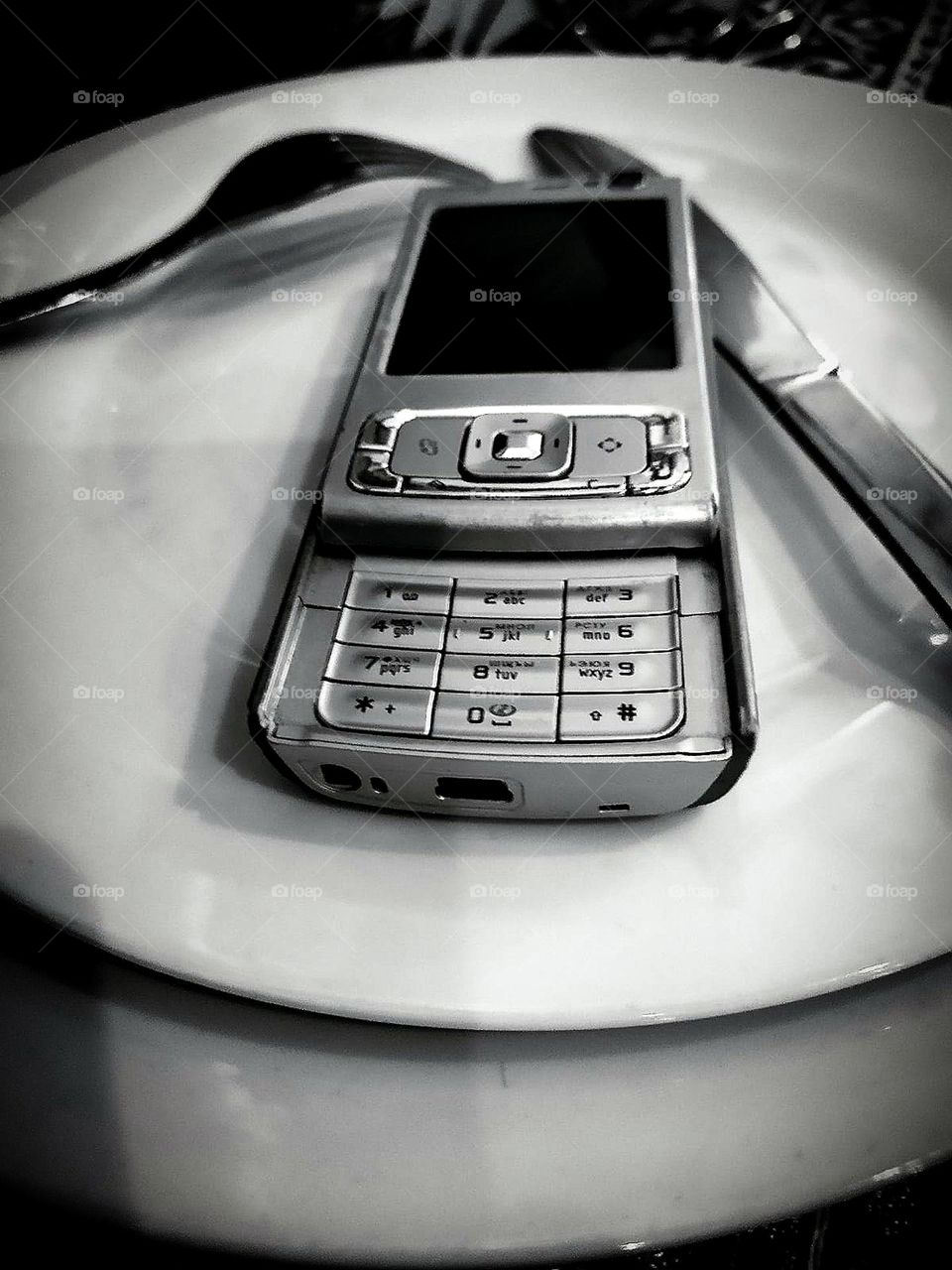 Black and white photo. Contrast. On the serving plates is an old push-button telephone: "Nokia 95". Fork and knife are on the plates