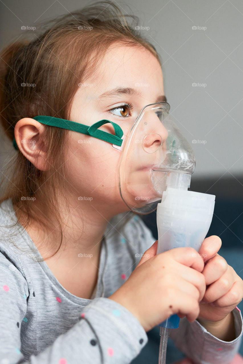 Doctor visiting little patient at home. Child having medical inhalation treatment with nebuliser. Woman wearing uniform and face mask