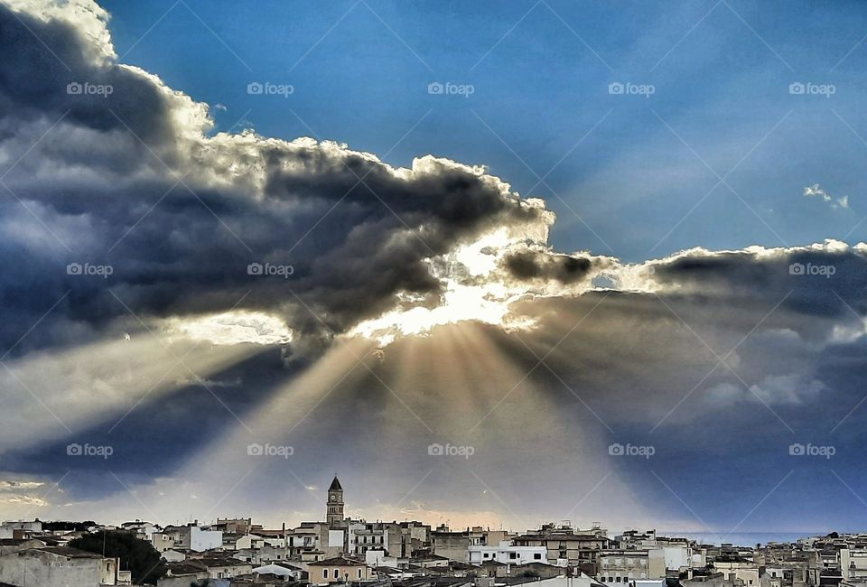 Porto Cristo, a town in the east of Mallorca under spectacular curtains of light projected by a hidden sun among a cloudy sky.