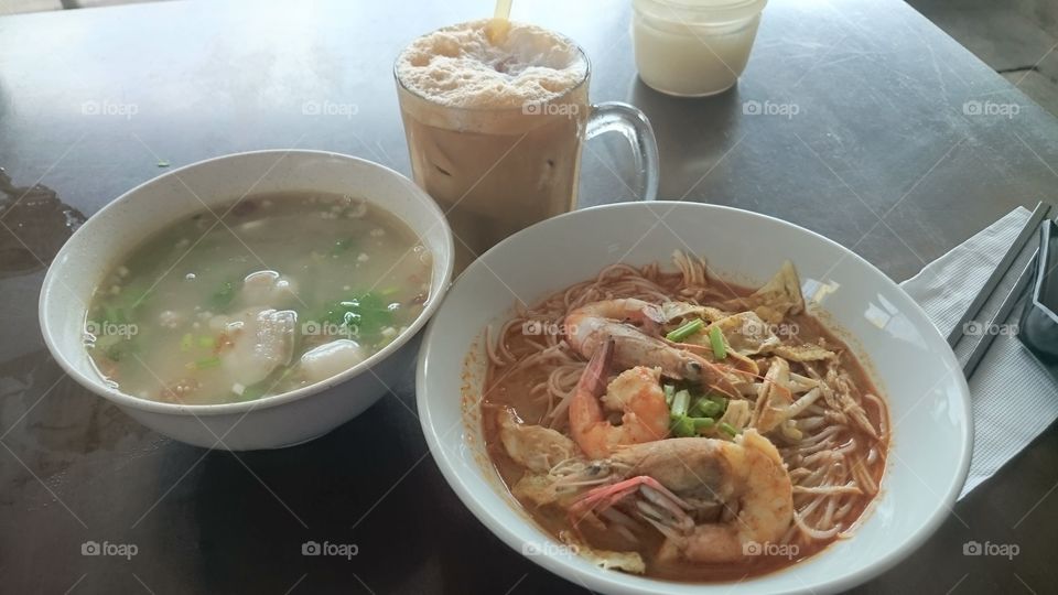 breakfast. A typical breakfast at a coffeeshop, also locally known as kopitiam. Iced coffee with milk, mixed pork soup and laksa.