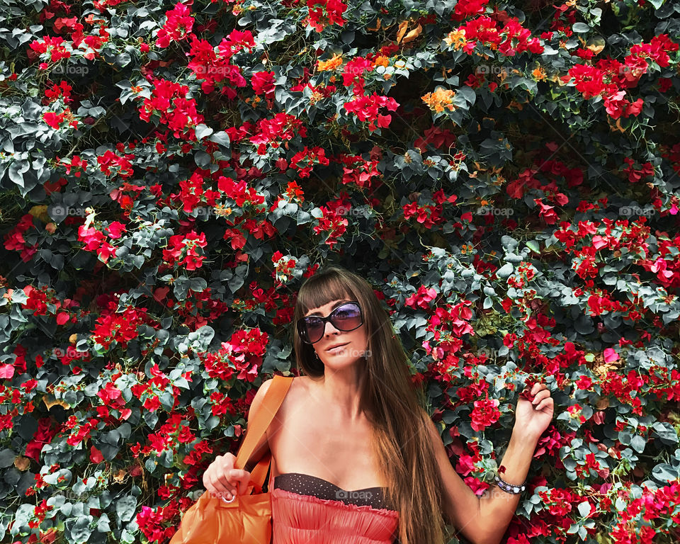 Young woman with long hair in front of pink flowering wall 