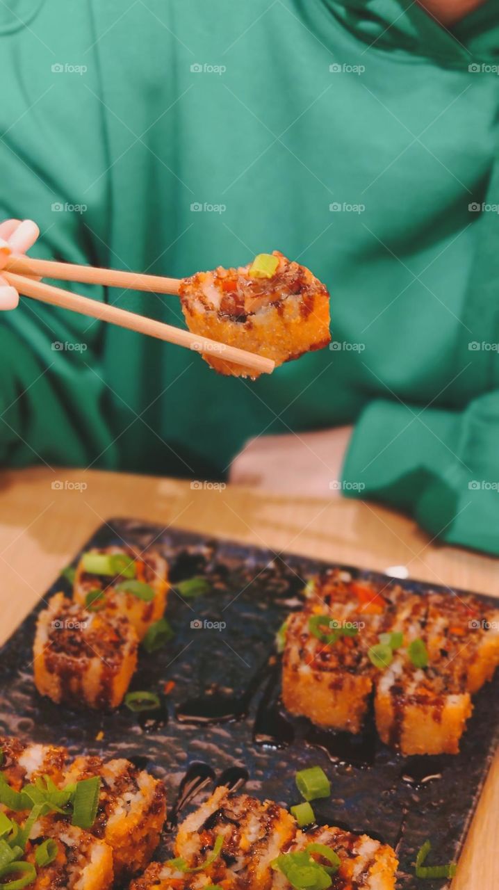 A young unrecognizable girl holds wooden sushi sticks over a plate while sitting at a table in an Asian restaurant in Brussels, close-up side view. Asian food concept.