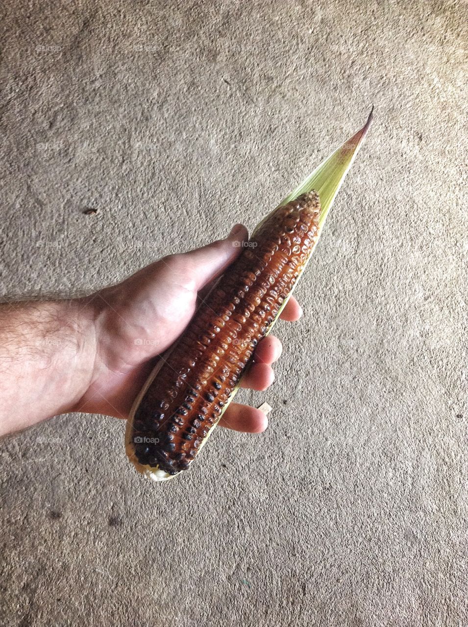 Person holding roasted corn on the cob