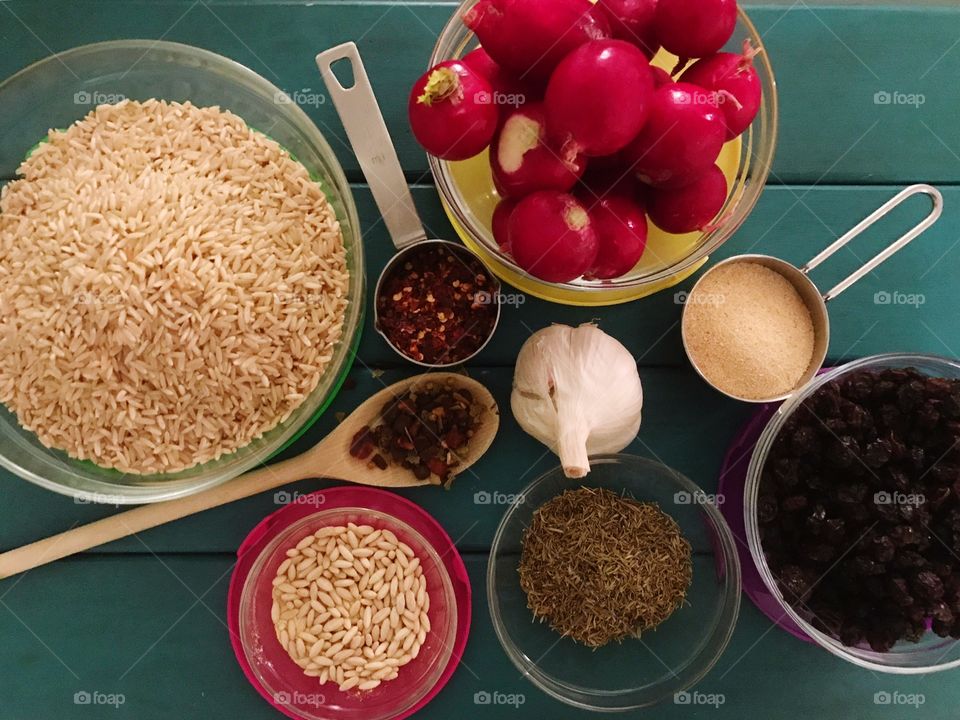 Fresh Herbs and spices for healthy cooking.. bowl of organic dry brown rice, bowl of fresh raisins, garlic cloves, garlic bulb, fresh red radishes , a wooden spoon with spicy hot pepper Herbs.  Measuring cup of garlic powder ..   