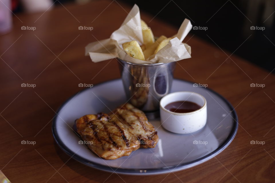 Delicious grilled chicken BBQ and french fries served on plate at a restaurant