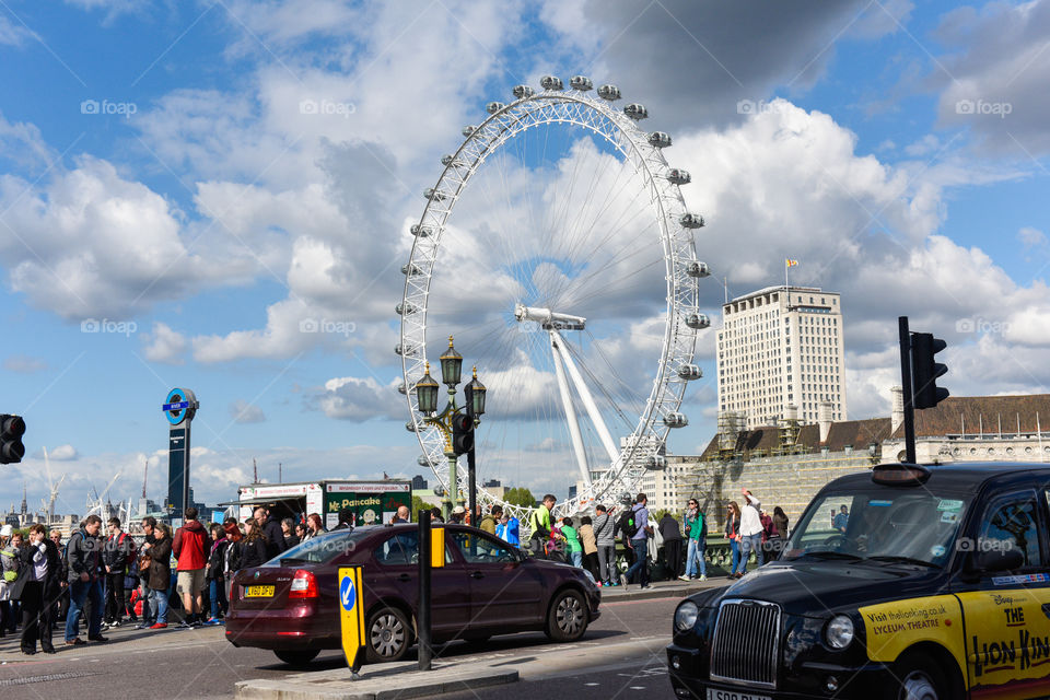London Eye from Westminister bridge with taxi and tourists.
