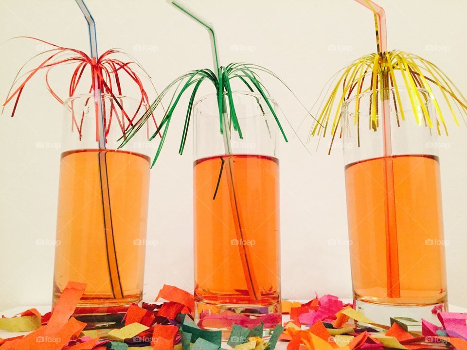 Three cocktails with decorated straws on a table with confetti