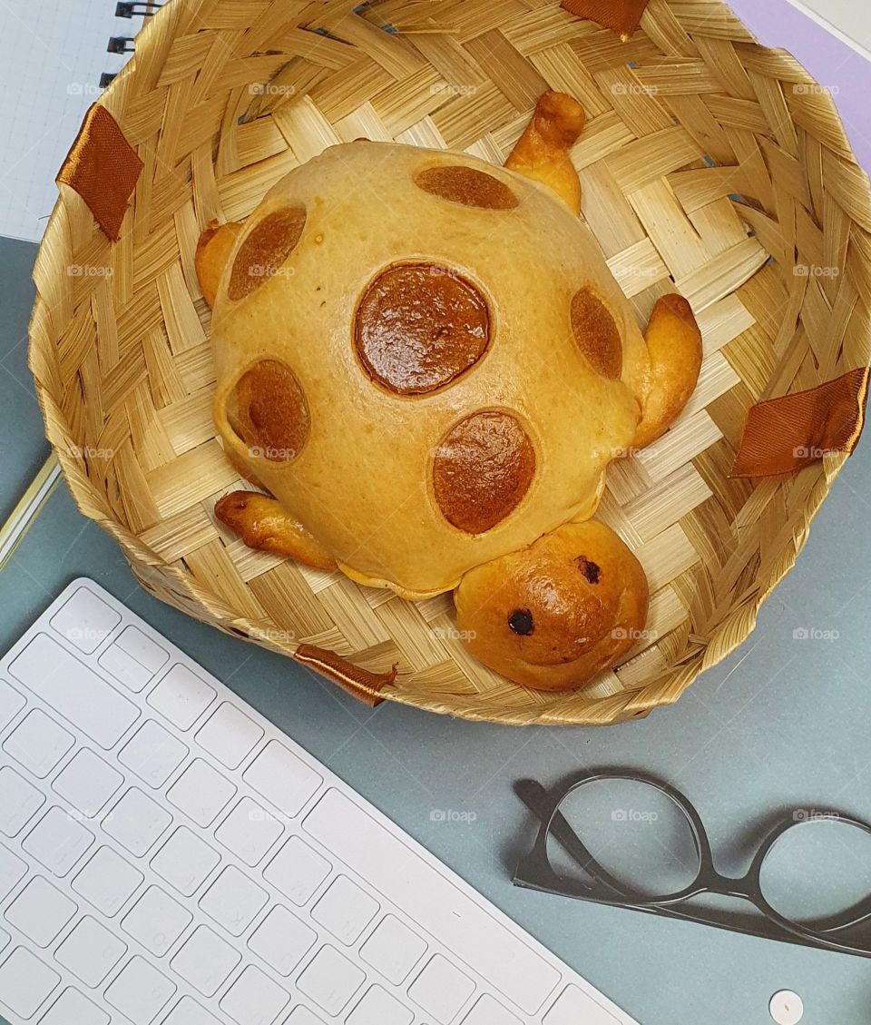 turtle-shaped bread is placed on a rattan plate,next to a computer keyboard and glasses